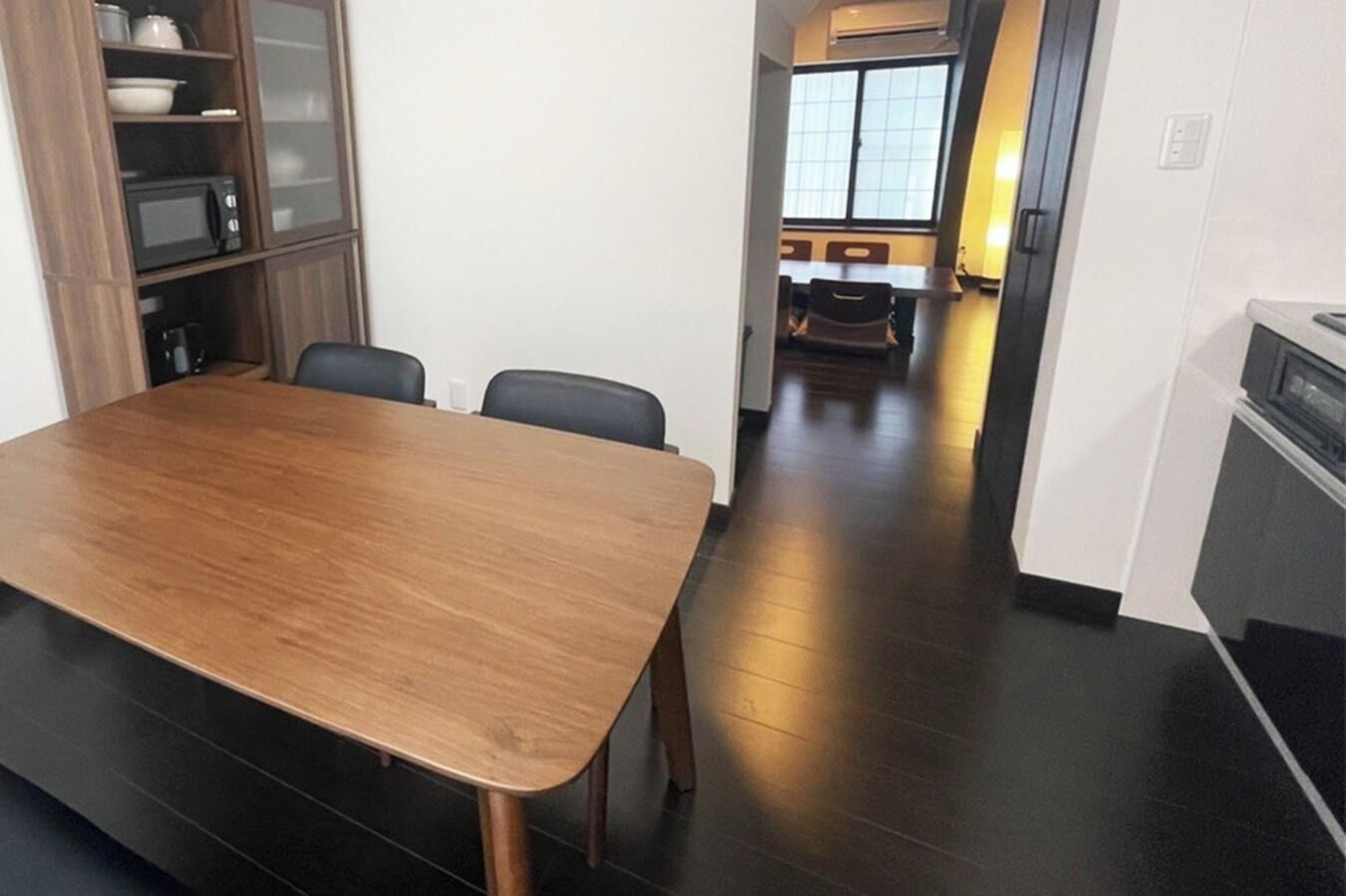 Cozinha moderna com mesa e cadeiras de madeira, micro-ondas embutido e armário com portas de vidro.