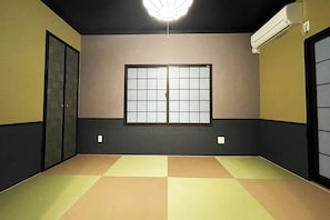 Una habitación con suelo de tatami, ventana con celosía de papel y ventilador de techo.