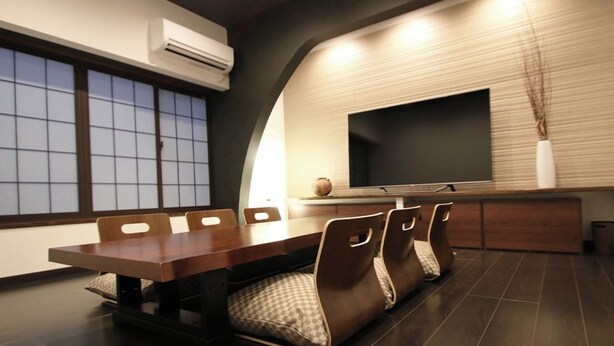 Un espace de repas moderne avec une longue table, des chaises rembourrées, un téléviseur à écran plat et un vase décoratif.