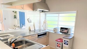A compact kitchen with a sink, stove, and microwave. There is a window with a view of the outdoors. - Rose Terrace Bise (Motobu)