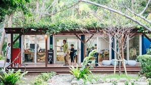 A small, rustic house with a wooden deck, a glass door entrance, and a garden area with rocks and plants. - Bise Nob's Village (Motobu)