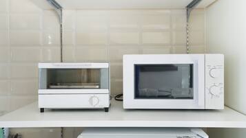 Two white microwave ovens on a white shelf against a tiled wall.