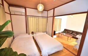 A room with two beds, a sofa, a table, and a ceiling light fixture. - T-reef Vacation House Pine Tree (Kamakura)