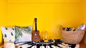 Une pièce avec un mur jaune, une guitare, une lanterne et un panier tressé posé sur un tapis à motifs.