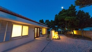 A modern house with a driveway, a well-lit entrance, and a garden area with a fire feature.