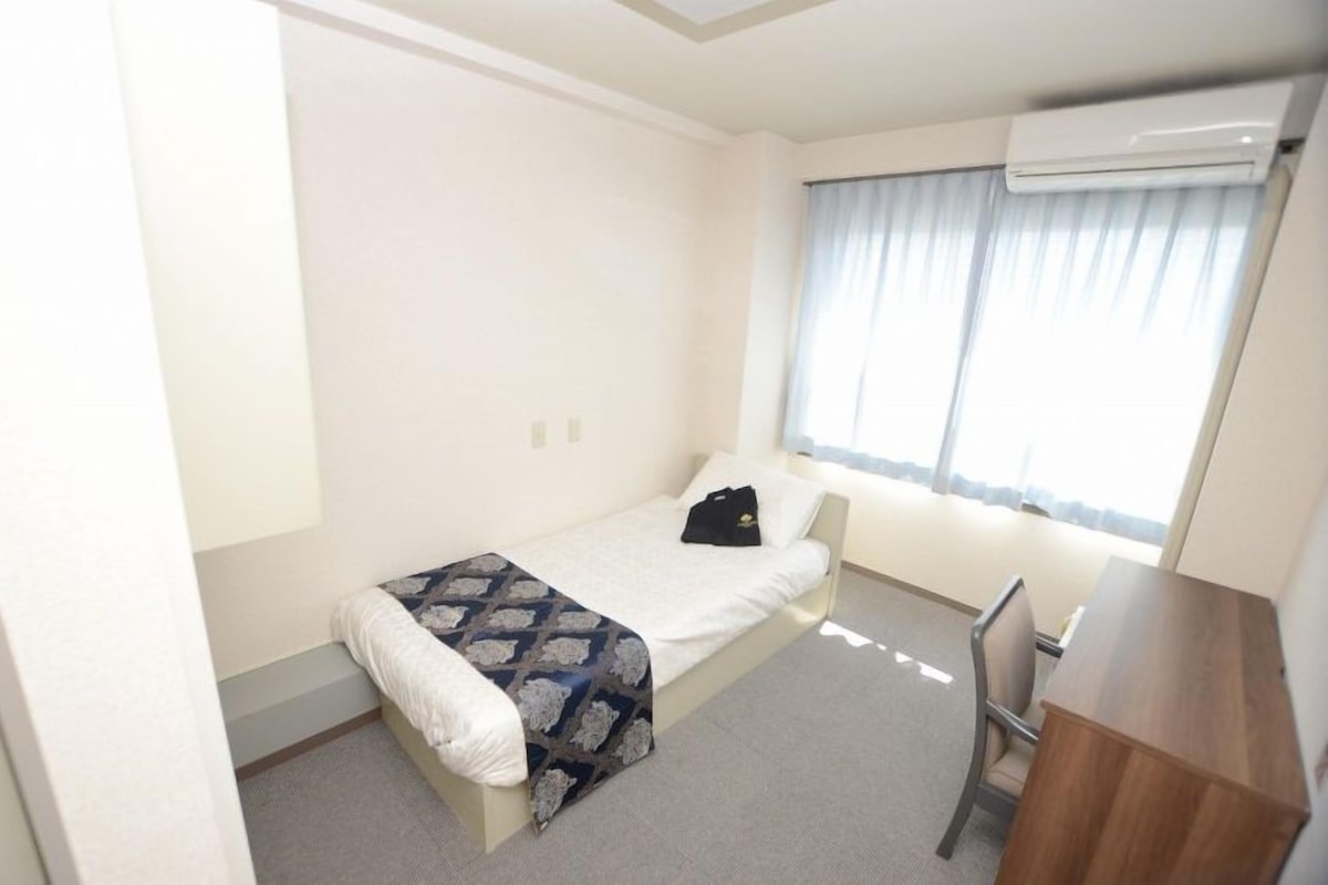 A small, neatly arranged bedroom with a single bed, a desk, and a chair.