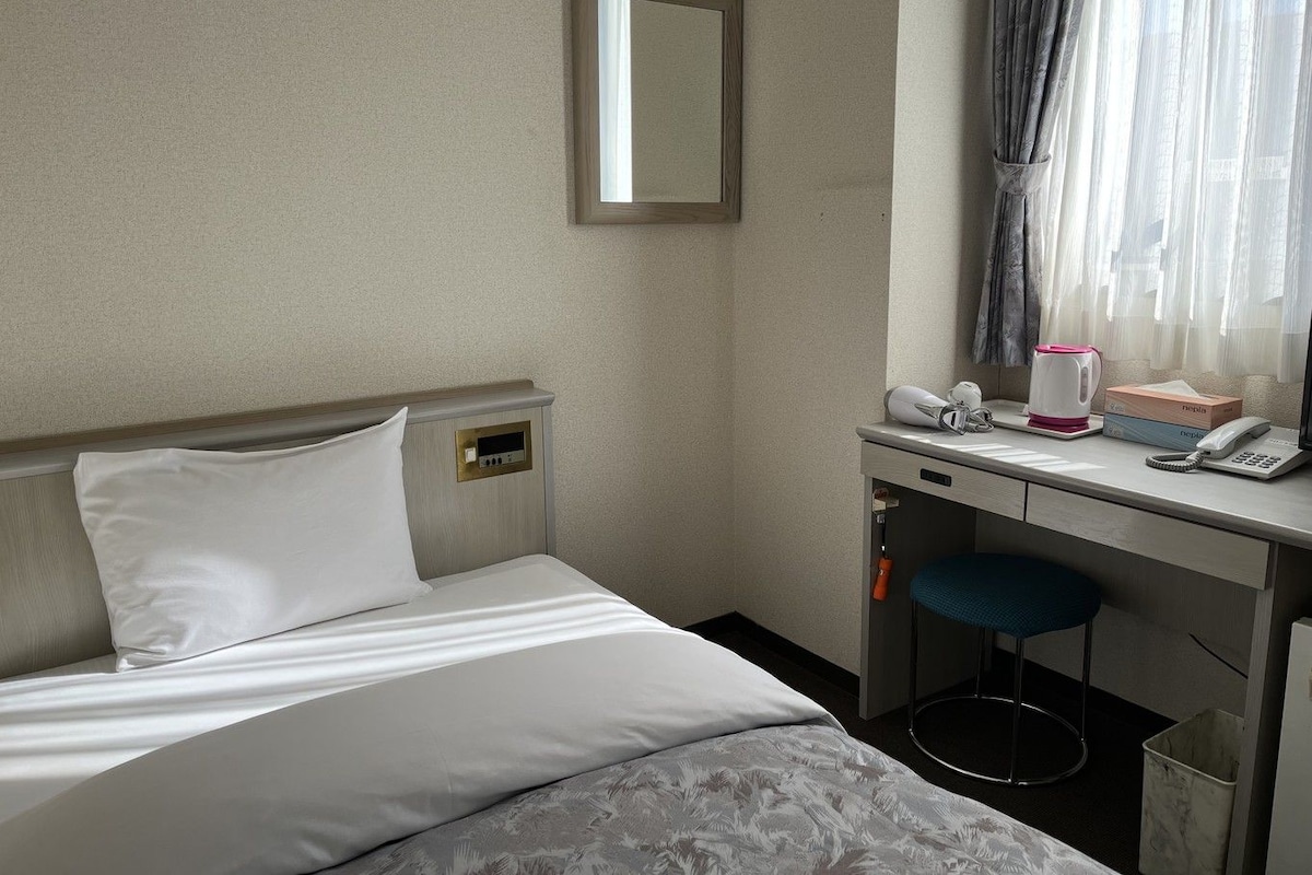 A hotel room with a bed, a desk with a telephone, a coffee maker, and a trash bin.