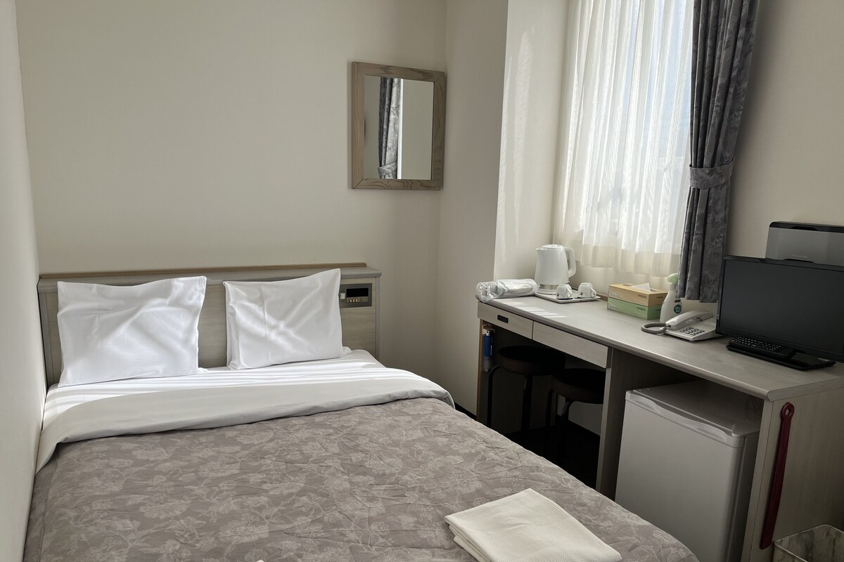 A hotel room with a bed, a desk with a computer, a telephone, and a television.