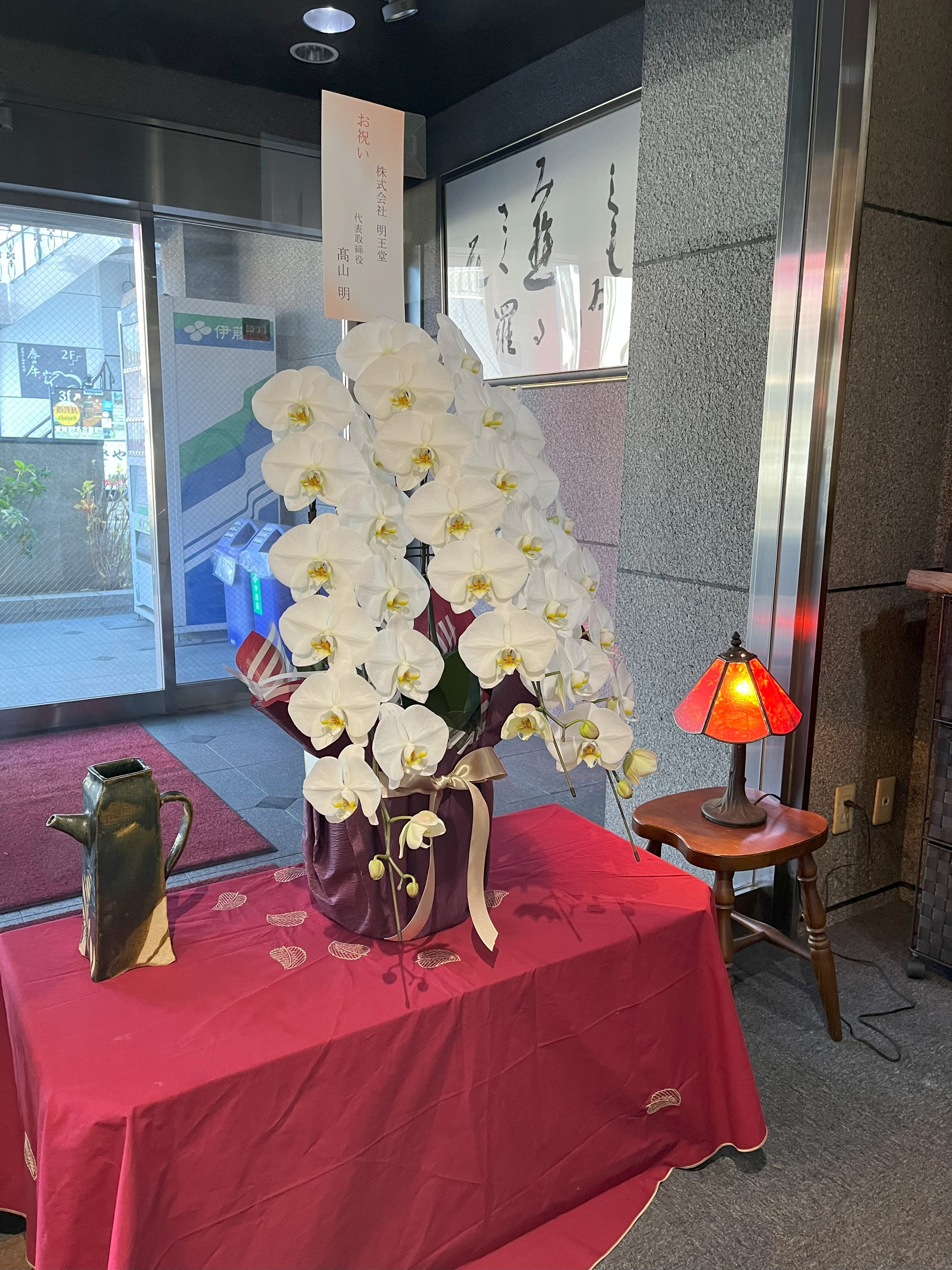 A table with a vase of white orchids, a decorative pitcher, and a small table lamp.