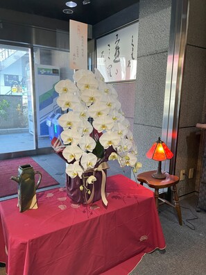A table with a vase of white orchids, a decorative pitcher, and a small table lamp. - Hotel Tetora Kasugai Station Hotel (Kasugai)