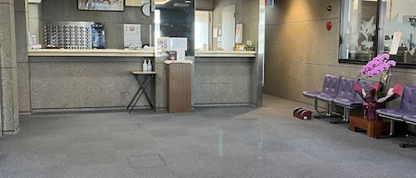 A hotel reception area with a counter, a cash register, and a seating area with purple chairs.