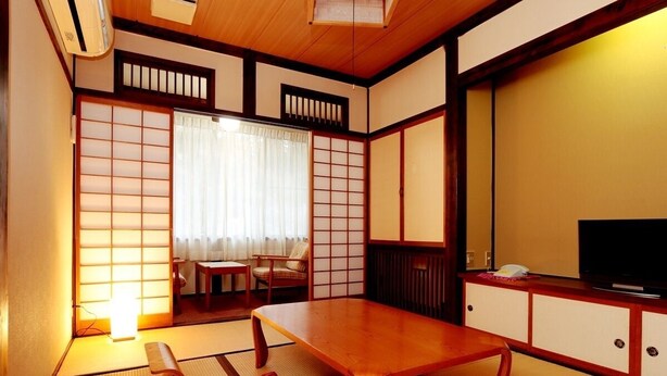 Ein traditioneller japanischer Raum mit Tatami-Böden, einem niedrigen Holztisch, einem Fernseher und Schiebetüren.