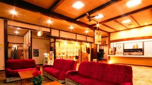 Eine Hotelhalle mit roten Sofas, Holztischen und einer Rezeption mit Theke und Dekorationselementen.