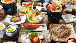 Eine Auswahl japanischer Gerichte, darunter Sushi, Sashimi und Nudeln, auf einem Tisch drapiert.