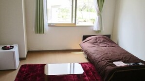 Ein kleiner, schlichter Raum mit einem Bett, einem Tisch und einem Fenster mit Vorhängen.