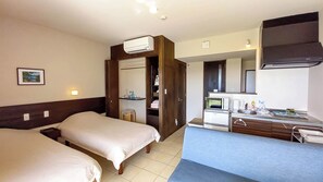 Une chambre d’hôtel avec deux lits, une kitchenette équipée d’un four à micro-ondes, d’une machine à café et d’un petit évier. On y trouve également une armoire avec un miroir et un tableau accroché au mur.