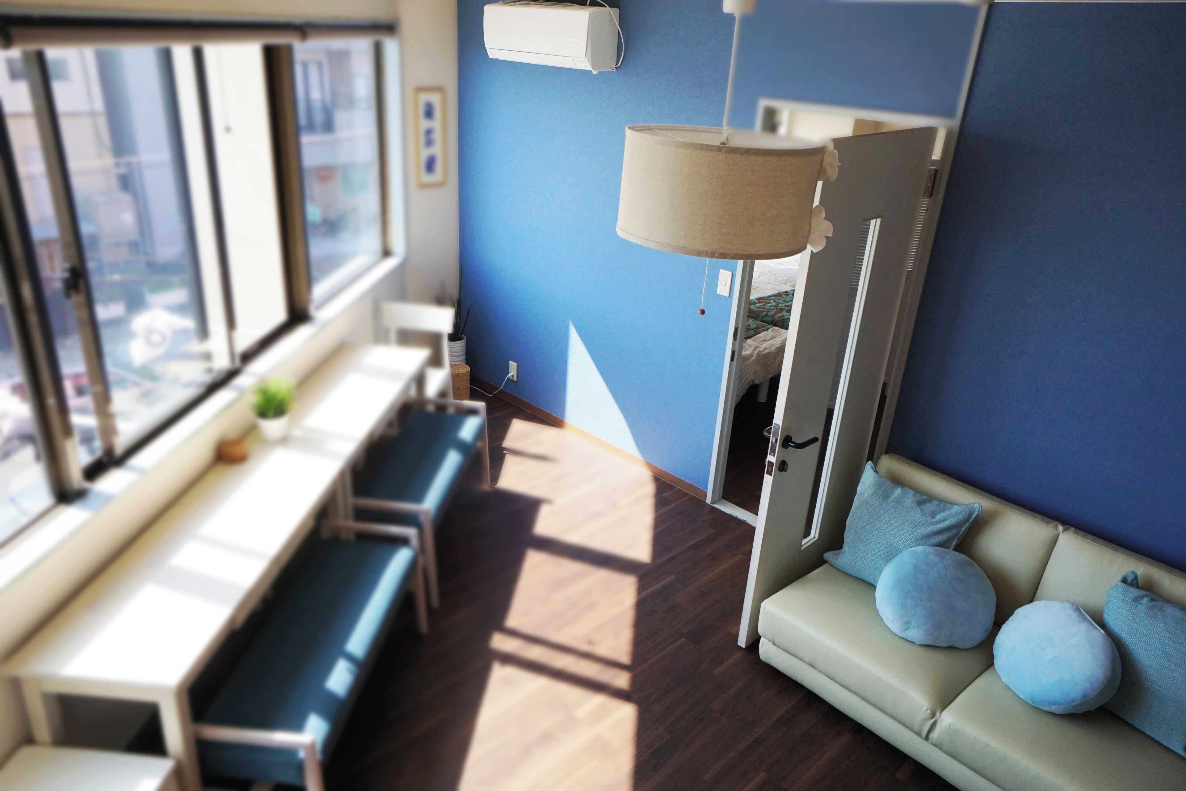 Una habitación con sofá, banca, mesa, lámpara y ventana con vistas.