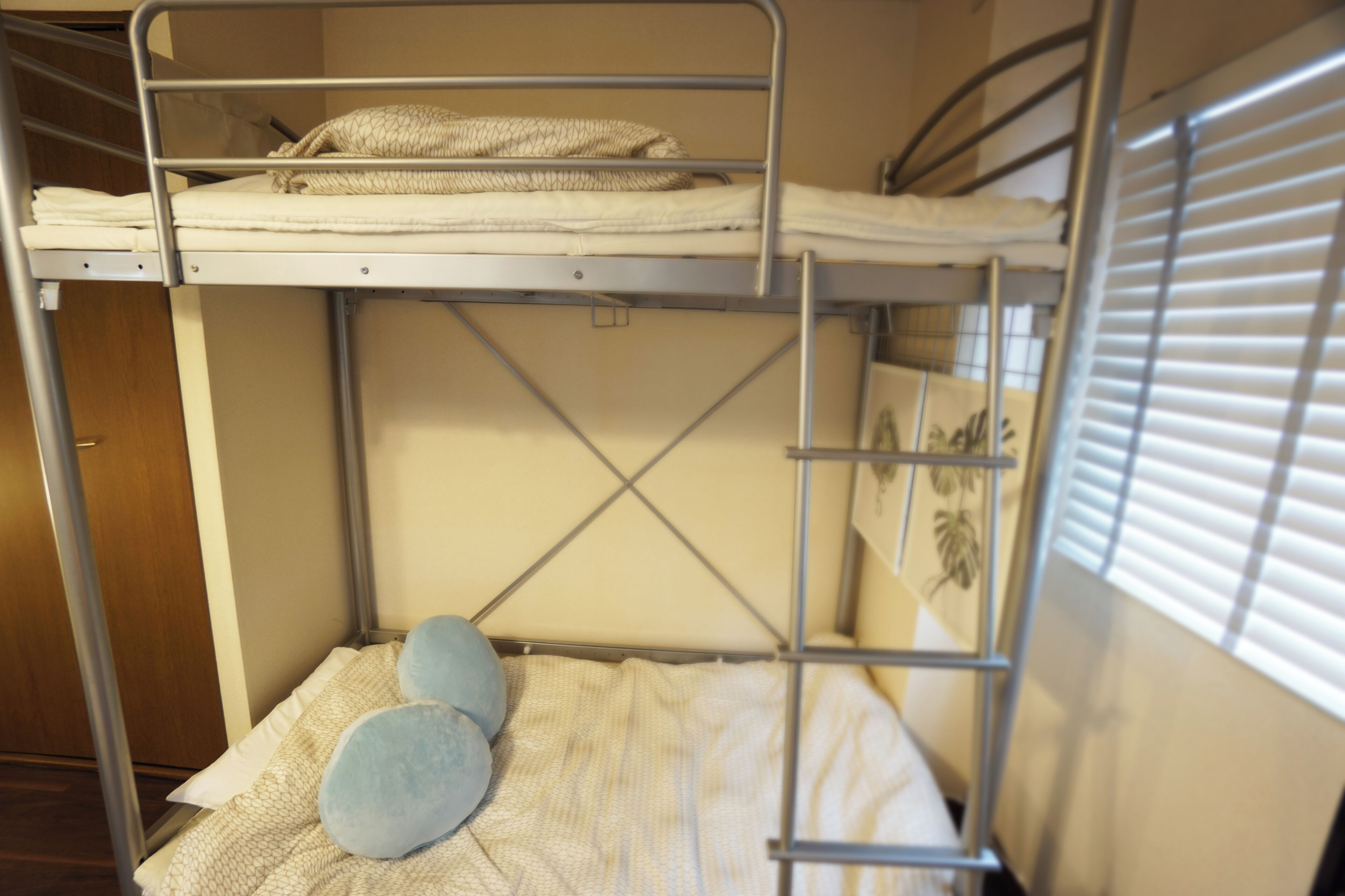 A bunk bed with a mattress and pillows, a window with blinds, and a door.