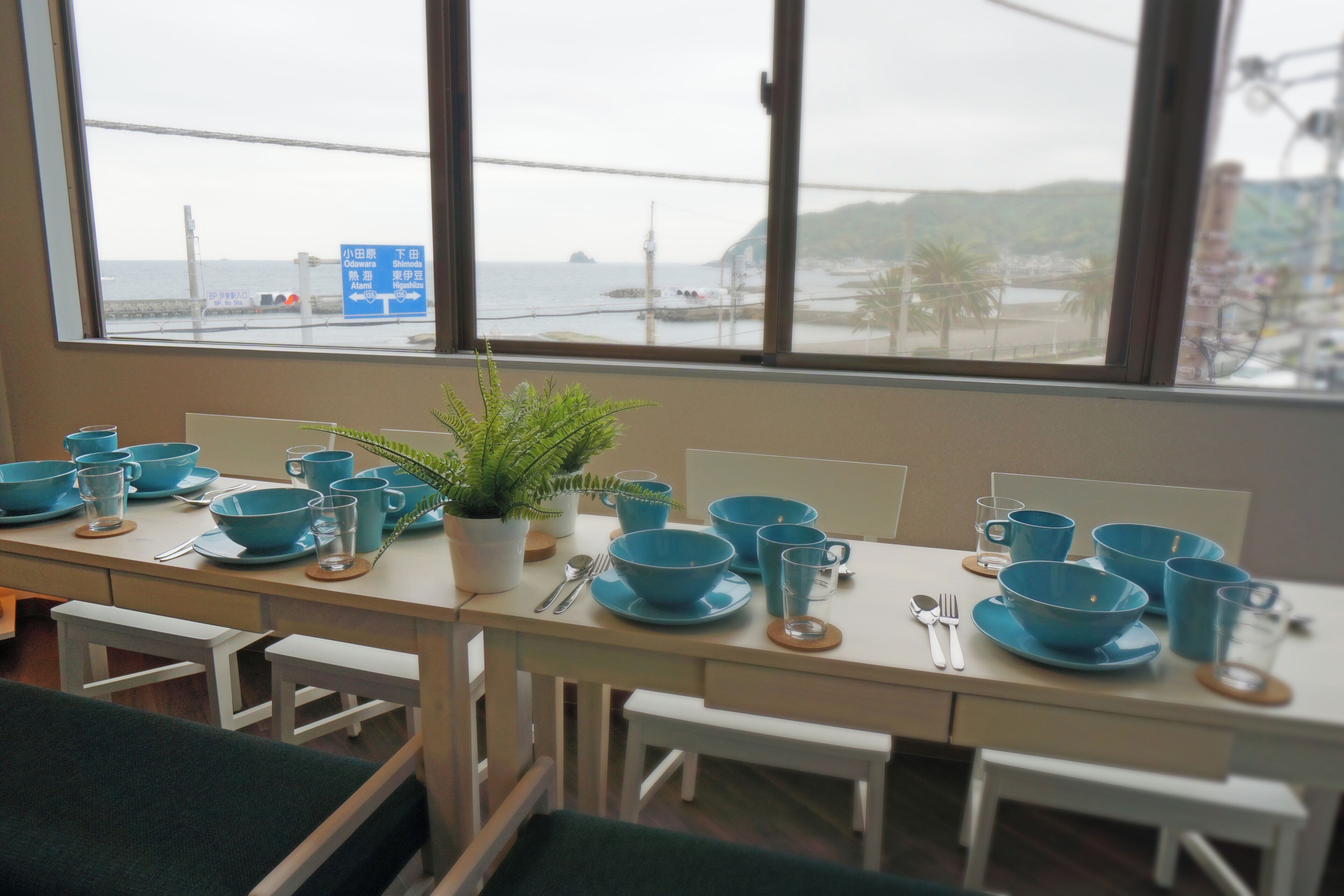 Un comedor con vistas al mar, una planta sobre la mesa y vajilla azul.
