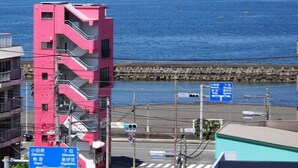 A coastal cityscape with a pink building, a clear blue sea, and a rocky breakwater. - Izu no Ie Moana (Ito)