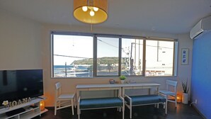 A living room with a large window, a flat-screen TV, a bench, and a table. - Izu no Ie Moana (Ito)