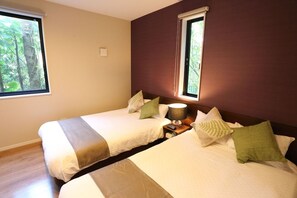 Une chambre d’hôtel avec deux lits, une table de chevet avec une lampe et une fenêtre donnant sur des arbres.