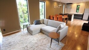 Un salon moderne avec un canapé d’angle, une table basse ronde et un coin repas avec des chaises orange.