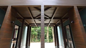 A covered walkway with wooden beams and brick walls, leading to a forested area.