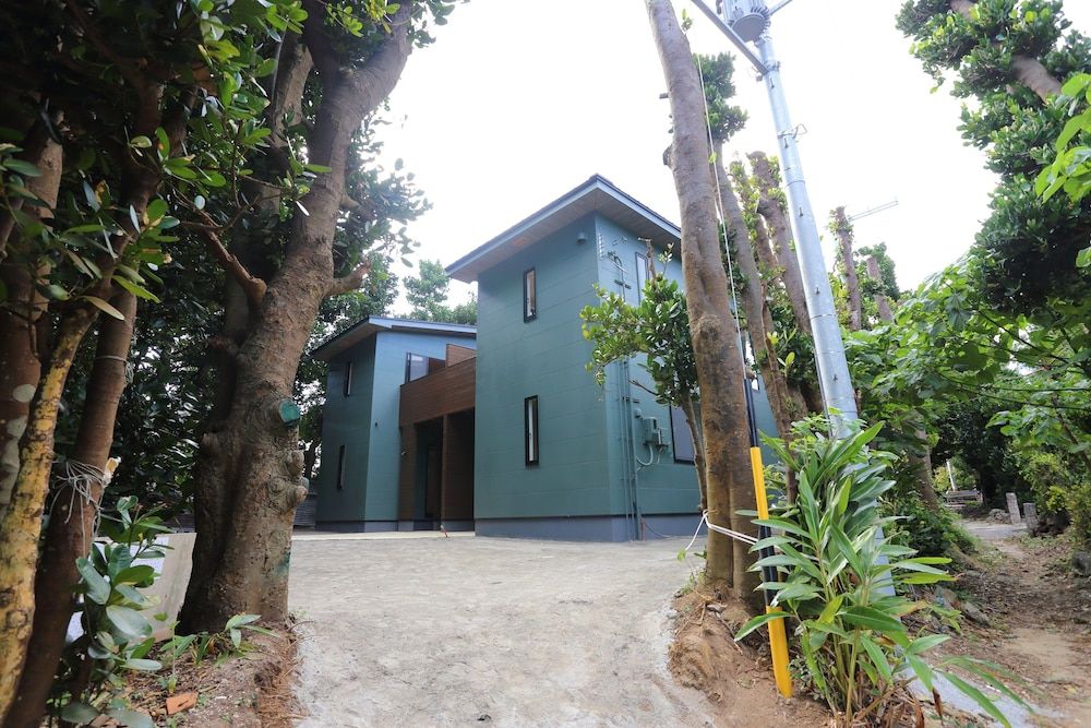 A modern building with a flat roof, surrounded by trees and a dirt path.