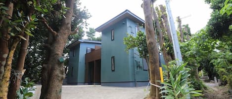 Un edificio moderno con techo plano, rodeado de árboles y un sendero de tierra.