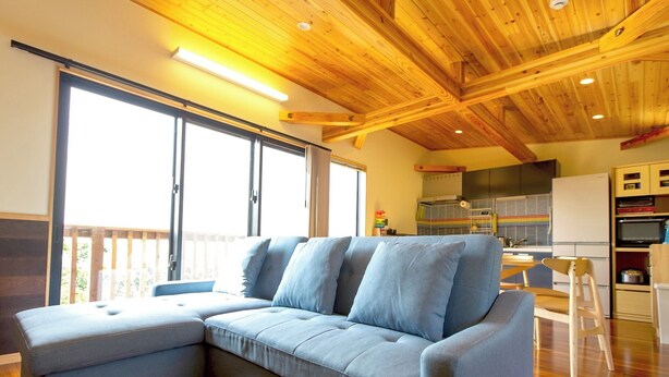 A modern living room with a sectional sofa, wooden ceiling beams, and a large window providing natural light. - Tenkyu Inn (Nanjo)