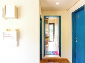 A hallway with a blue door, a framed certificate on the wall, and a colorful rug leading to a room. - Tenkyu Inn (Nanjo)