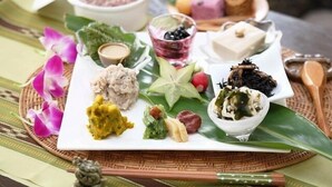 Un plateau contenant divers aliments, notamment une variété de trempettes, des fruits et un petit bol de thé, le tout disposé sur une assiette blanche ornée d’une feuille verte.