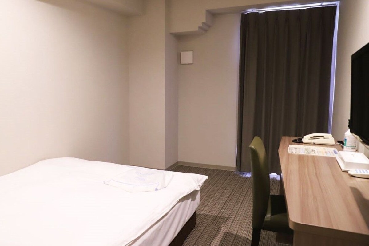 A hotel room with a single bed, a desk with a telephone, and a window with curtains.
