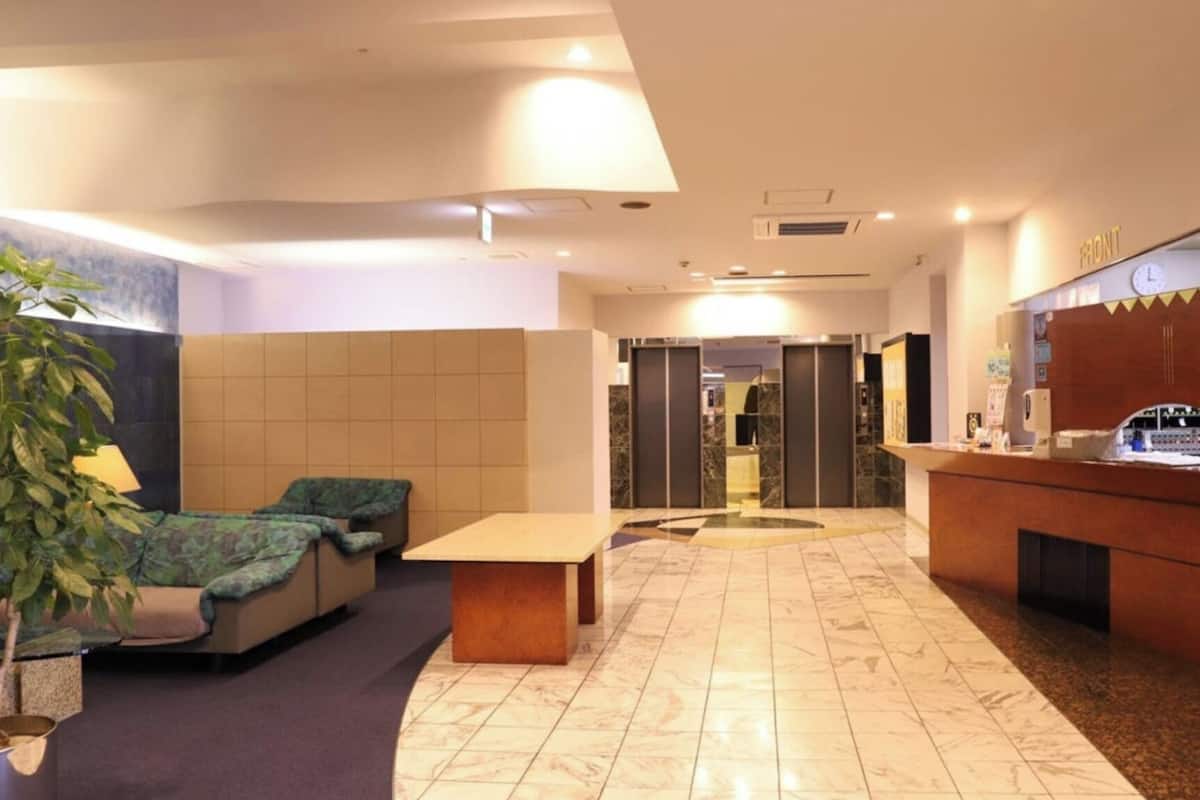Um saguão de hotel com balcão de recepção, área de estar e uma planta.