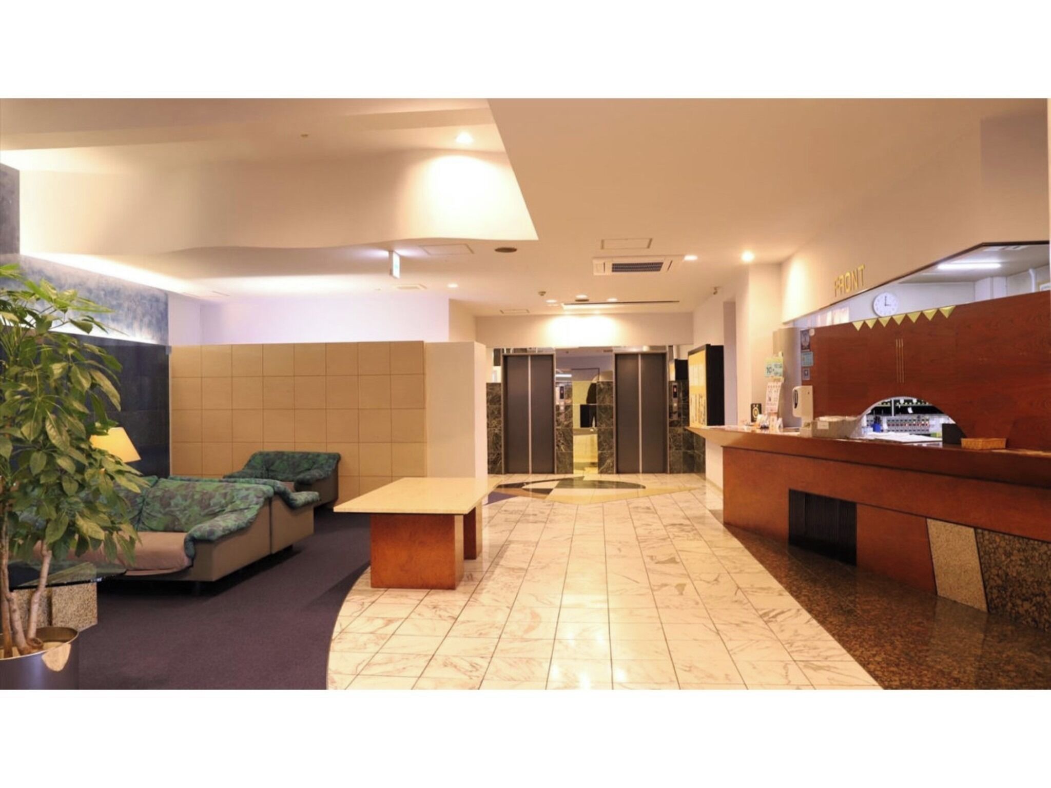 Un vestíbulo de hotel con mostrador de recepción, zona de estar y una planta en maceta.