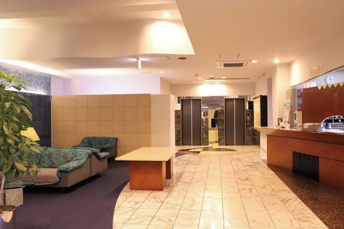 A hotel lobby with a reception desk, seating area, and a potted plant.