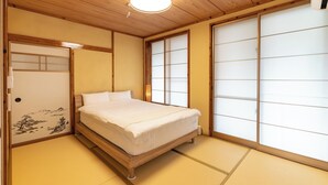 A traditional Japanese-style bedroom with tatami flooring, a wooden bed, sliding shoji doors, and a ceiling light fixture. - Green Beach Iejima <iejima> (Ie)