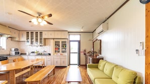 A spacious kitchen with wooden flooring, a dining table, and a green sofa. - Green Beach Iejima <iejima> (Ie)