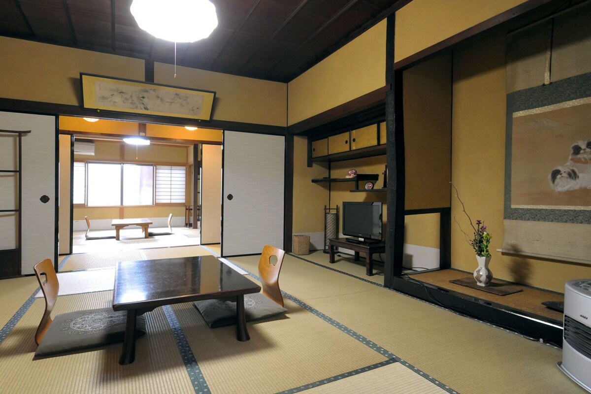 A traditional tatami mat room with a low table and chairs, a television, and a painting on the wall.