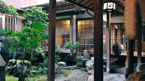 Een traditionele Japanse tuin met een houten constructie, stenen lantaarns en verschillende planten.