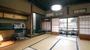 Een traditionele Japanse kamer met tatami vloeren, een televisie op een lage standaard, een tafel met stoelen op tatami matten, en een uitzicht door een shoji schuifdeur.