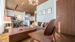 Ein modernes Wohnzimmer mit Holzboden, einer Couch, einem Couchtisch und einem Essbereich im Hintergrund.