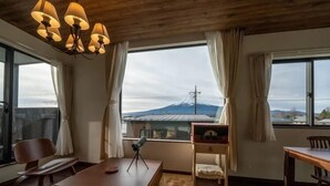 Ein Zimmer mit Holzboden, großen Fenstern mit Vorhängen, einem Holztisch, einem Stuhl und einem Teleskop.