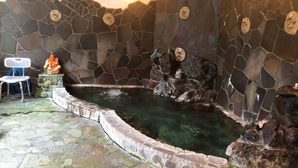 Un hidromasaje con paredes de piedra y una fuente de agua cristalina, rodeado de suelo y paredes de piedra.