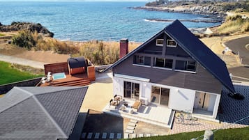 A modern house with a large deck, a swimming pool, and a view of the ocean.