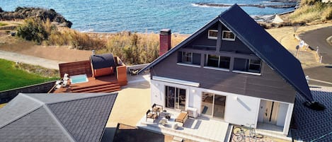 A modern house with a large deck, a swimming pool, and a view of the ocean.