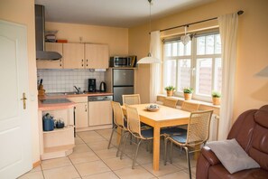 A compact kitchen with a dining area, featuring a microwave, stove, and a dining table with chairs. - Strandstr. 4b "Likedeeler 2" - "Likedeeler 2" Vacation Home in Zingst: 95 m², (Zingst)