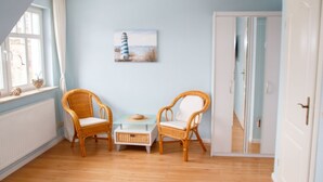 Ein Zimmer mit zwei Korbstühlen, einem kleinen Tisch und einem Gemälde eines Leuchtturms an der Wand.