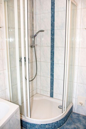 A glass-enclosed shower with a white bathtub, blue-tiled accents, and a white tiled floor. - Strandstr. 4b "Likedeeler 2" - "Likedeeler 2" Vacation Home in Zingst: 95 m², (Zingst)